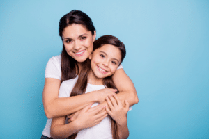 Smiling mother hugging her young daughter against a blue background.
