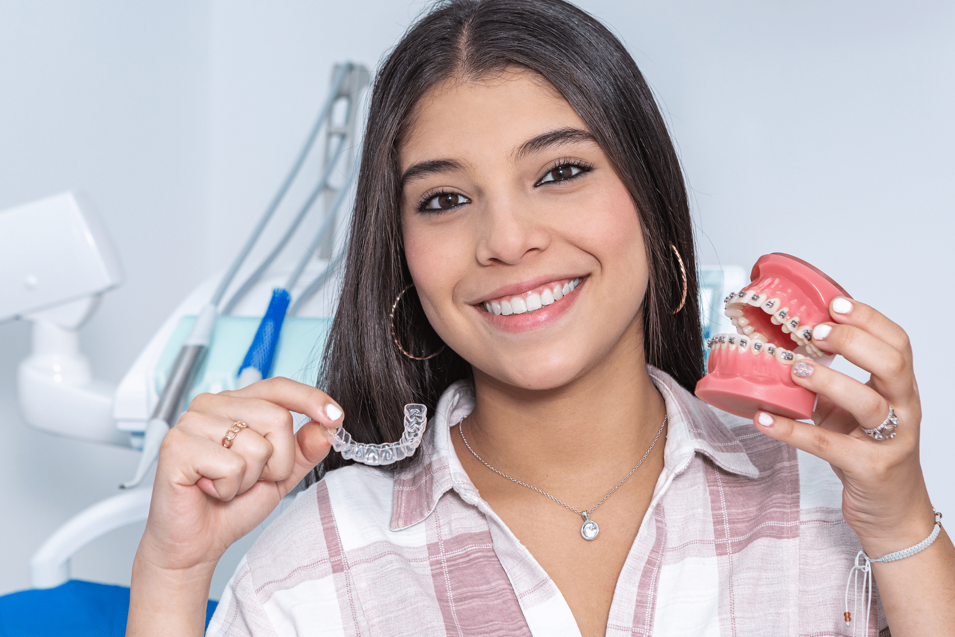 Smiling young woman holding a clear aligner tray and a dental model with braces