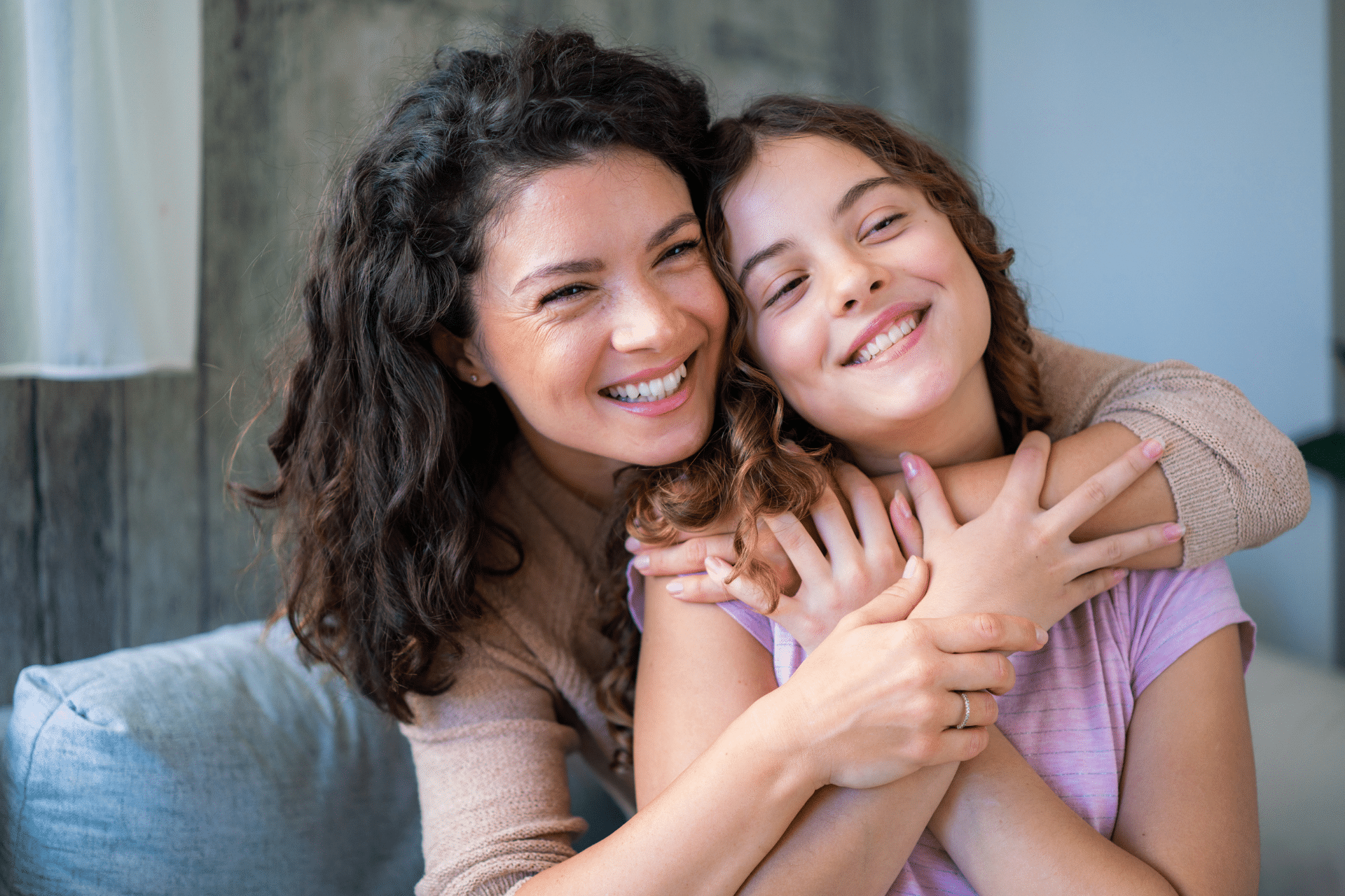 Smiling mother and young daughter hugging closely indoors